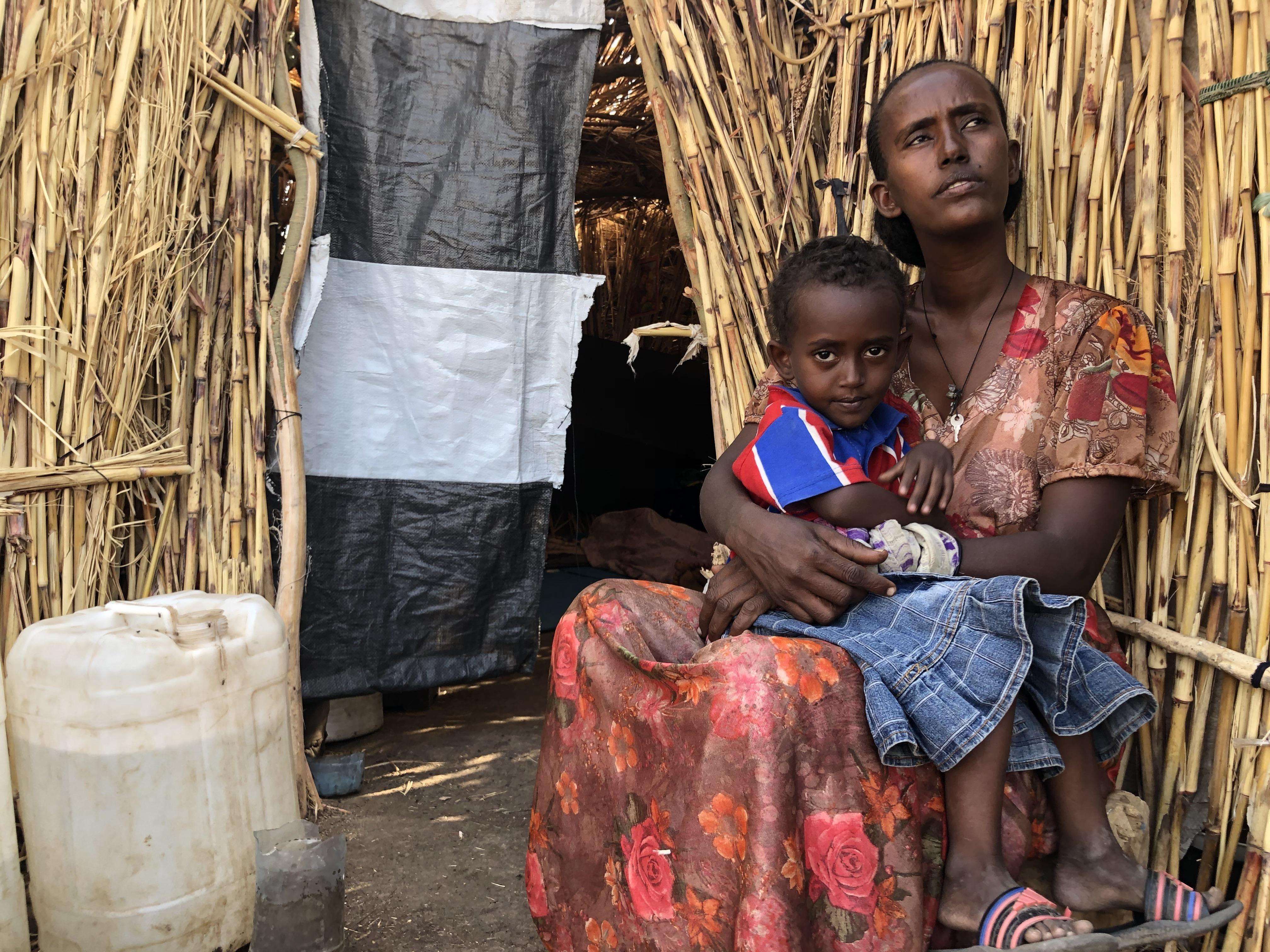 Mother with her child in front of a straw shelter