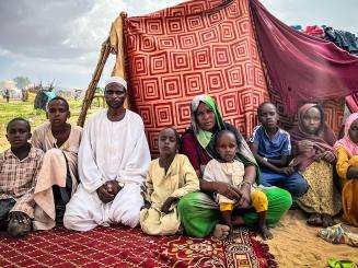 A family of Sudanese refugees sit in front of a makeshift tent in a refugee camp in Chad