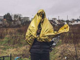 A young migrant covers himself with a survival blanket on a rainy day in Calais.