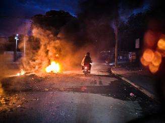 A person rides a motorcycle through fire in Haiti.