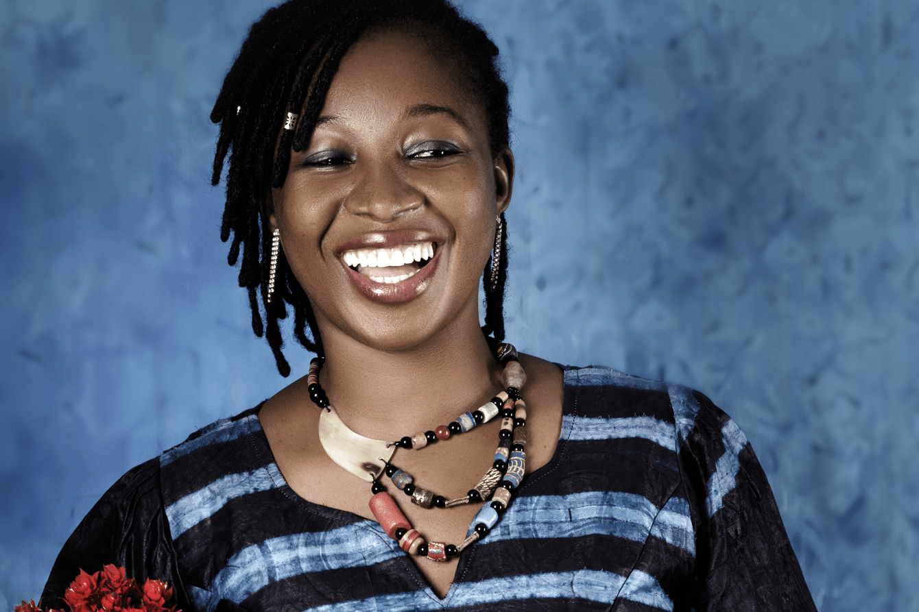 A woman smiling against a blue background holding a bouquet of red flowers. 