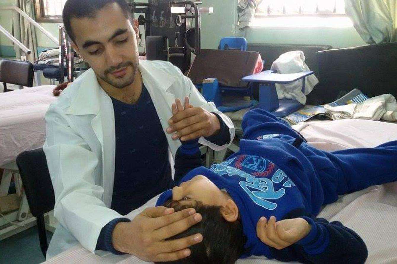 MSF Physiotherapist Fadi Al-Wadiya does exercises with a young patient.