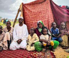 A family of Sudanese refugees sit in front of a makeshift tent in a refugee camp in Chad